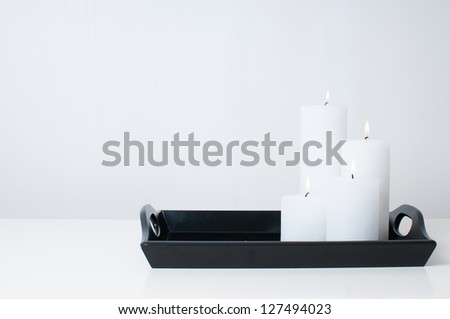 Four white candles burning on a black tray on a white table in an interior