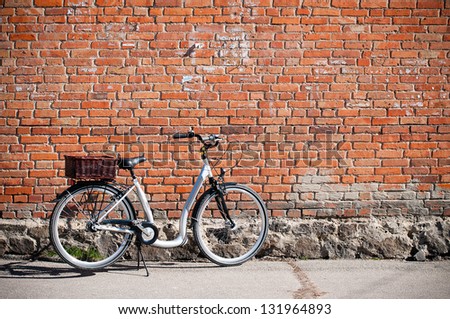 New city bicycle with basket standing near the brick wall on a pavement in the street