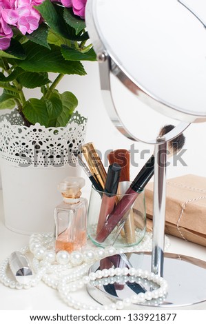 Beauty and make-up concept: table mirror, flowers, perfume, jewelry and makeup brushes on a white table, close-up