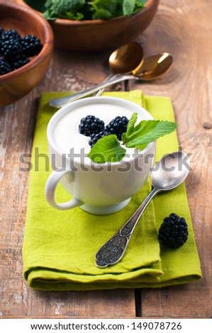 Healthy breakfast, creamy yogurt with blackberries, fruit cream dessert in a cup on a green napkin, on a wooden board in a rustic vintage style.