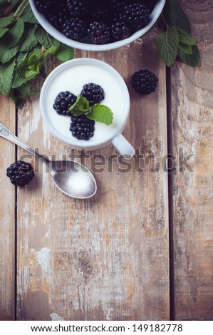 Healthy breakfast, creamy yogurt with blackberries, fruit cream dessert in a cup, on a wooden board in a rustic vintage style.