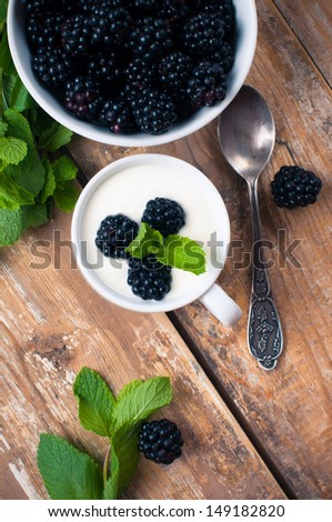 Healthy breakfast, creamy yogurt with blackberries, fruit cream dessert in a cup, on a wooden board in a rustic vintage style.
