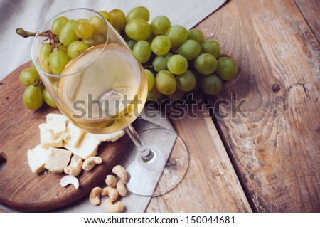 A glass of white wine, grapes, cashew nuts and soft cheese on a wooden board, rustic style background