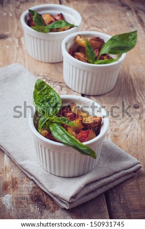 Vegan food: roasted vegetables, tomatoes, potatoes and peppers with fresh basil in ceramic forms on a wooden board