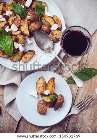 Homemade rustic dinner: a glass of wine and a baked potato with soft cheese and fresh basil in a white plate on a wooden board