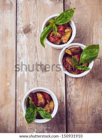 Vegan food: roasted vegetables, tomatoes, potatoes and peppers with fresh basil in ceramic forms on a wooden board