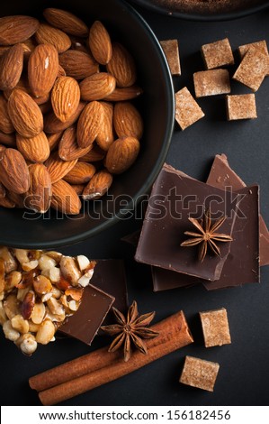 Black and milk chocolate, nuts, sweets, spices and brown sugar on a black background, food concept