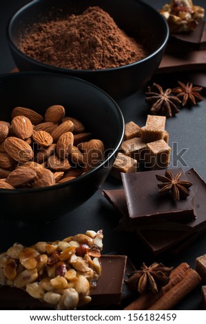 Black and milk chocolate, cocoa powder, nuts, sweets, spices and brown sugar on a black background, food concept