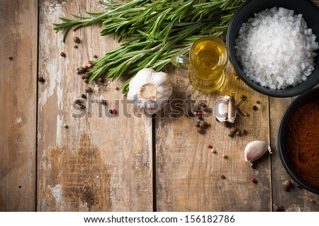 Different spices, rosemary, allspice, garlic, oil and salt on a wooden board, rustic kitchen background