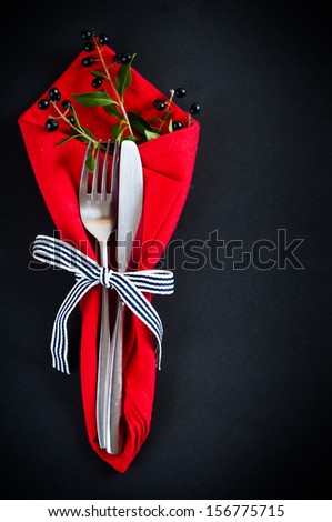 Autumn table setting with wild grapes, dried herbs and berries in a napkin with a ribbon, plate, fork and knife on a black background