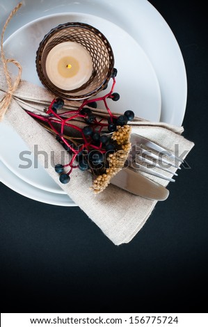 Autumn table setting with wild grapes, dried herbs and berries in a napkin, plate, fork and knife on a black background