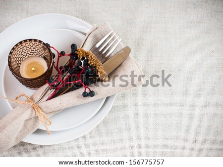 Autumn table setting with wild grapes, dried herbs and berries in a napkin, plate, fork and knife on a beige linen tablecloth