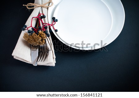 Autumn table setting with wild grapes, dried herbs and berries in a napkin, plate, fork and knife on a black background