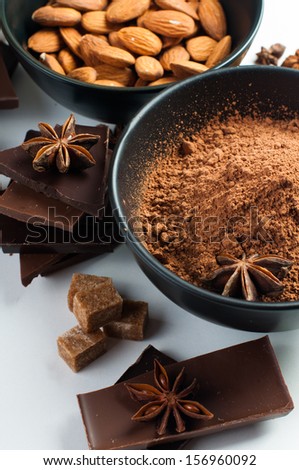 Black and milk chocolate, cocoa powder, nuts, sweets, star anise, cinnamon and brown sugar on a white background, closeup, sweets concept