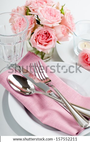 Luxurious table setting with pink roses, candles and shiny new cutlery on a white background, isolated