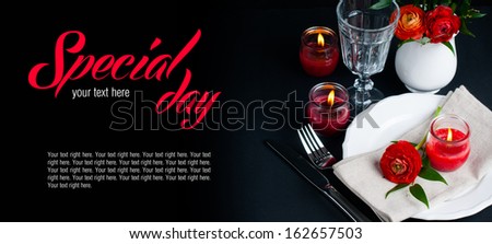 Festive dining table setting with red buttercup flowers, candles, napkins and shiny new cutlery on a black background