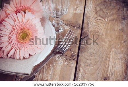 Vintage dining table setting with pink gerberas, napkin and cutlery on a wooden board, close-up