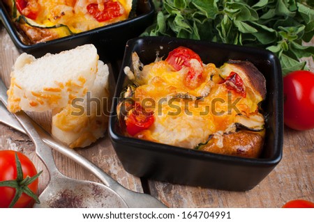 Two dishes of vegetable casserole with cheese, zucchini, cherry tomatoes and oregano on a rustic wooden board with vintage cutlery, home cooking