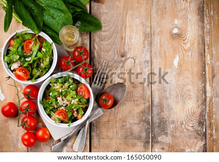 Dietary food background: vegetable salad with spinach, cherry tomatoes, barley porridge and olive oil on an old wooden board, vegan cuisine