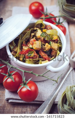 Dietary green pasta with vegetables, spinach, zucchini and cherry tomatoes in a white ceramic pot on a wooden table, fresh rural lunch in a rustic style