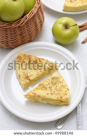 Two pieces of apple pie on a white plate and a basket of apples