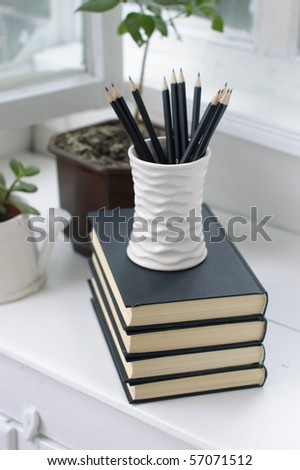A stack of books, flowers and pencils in a cozy white verandah