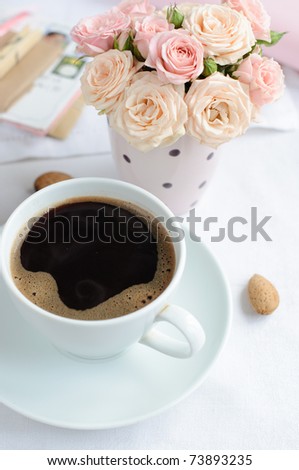 cup of coffee and a bouquet of delicate pink roses on the table in the morning