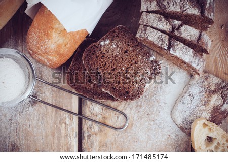White french baguette and fresh rustic loaf of wholemeal rye bread, sliced Ã?Â¢??Ã?Â¢??and flour on a wooden board, bakers, food background is.