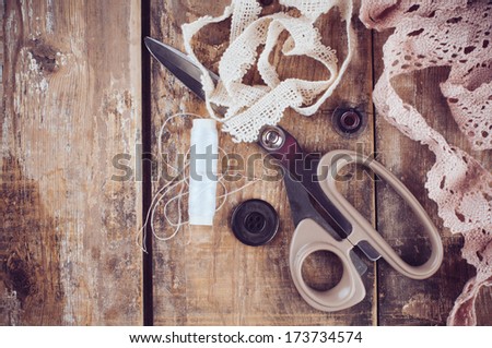Rustic sewing background: scissors, thread, fabric and lace on an old wooden board, hand-made and crafts, close up