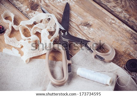 Rustic sewing background: scissors, thread, fabric and lace on an old wooden board, hand-made and crafts, close up