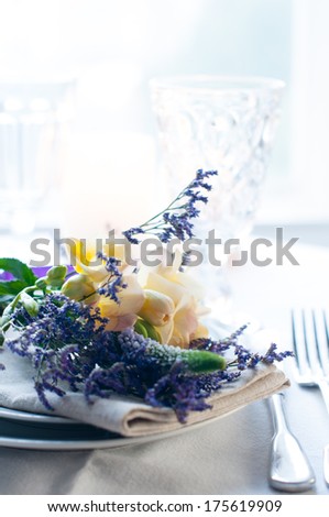 Festive dining table setting with a bouquet of yellow and purple freesias flowers, crockery and cutlery, on white background, daylight.