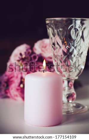 Vintage festive decorations, pink burning candle, crystal glass and bouquet of pink roses in the background.