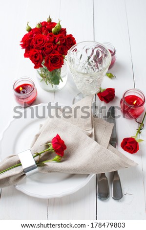 Festive table setting with red roses and candles on white wooden table, rustic style