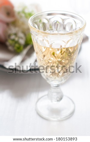 Glass of white wine and festive fine dining table setting with a bouquet of flowers on a white table