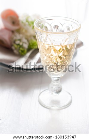 Glass of white wine and festive fine dining table setting with a bouquet of flowers on a white table