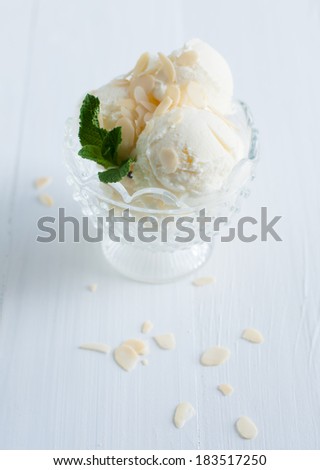 Creamy vanilla ice cream with almonds and mint leaves in a crystal bowl on a white wooden board, sweet summer dessert, homemade food.