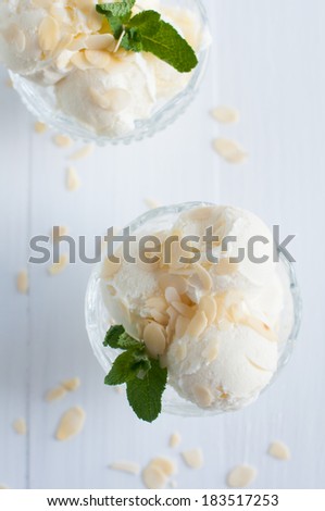 Creamy vanilla ice cream with almonds and mint leaves in a crystal bowl on a white wooden board, sweet summer dessert, homemade food.