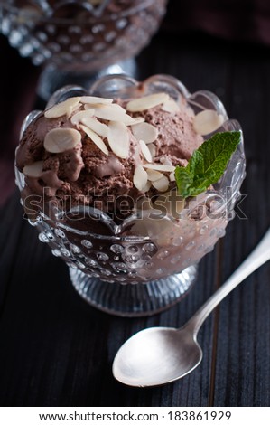 Two portions of delicious chocolate ice cream with almonds and mint leaf in crystal bowls and dark brown cloth on a wooden board, appetizing dessert, food closeup.