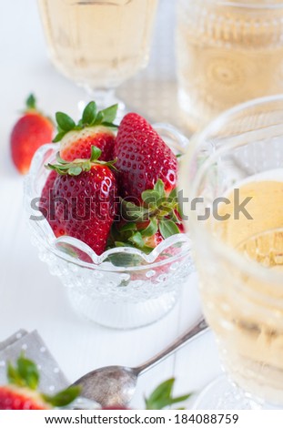 Natural fresh strawberries in a crystal bowl and a few glasses of white wine on a wooden board, drinks and dessert of summer berries.
