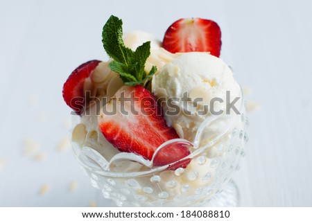 Creamy vanilla ice cream with almonds, fresh strawberries and mint leaves in a crystal bowl on a white wooden board, sweet summer dessert, homemade food.