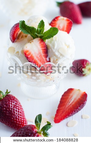 Creamy vanilla ice cream with almonds, fresh strawberries and mint leaves in a crystal bowl on a white wooden board, sweet summer dessert, homemade food.
