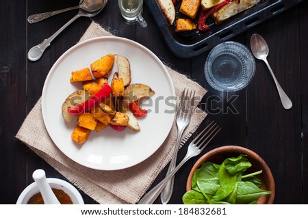 Healthy vegetarian food, roasted vegetables, peppers, potatoes and pumpkin. Dish on a plate, spices, herbs and drinks on the table.