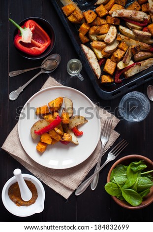 Healthy vegetarian food, roasted vegetables, peppers, potatoes and pumpkin. Dish on a plate, spices, herbs and drinks on the table.