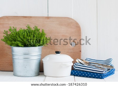 Cottage life, country kitchen decoration: a house plant in a metal pot, kitchen pottery, utensils and napkins on white painted board. Cozy home country life background is.