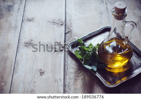 Fresh olive oil in a vintage bottle and bunch of green basil on a metal tray on a wooden board