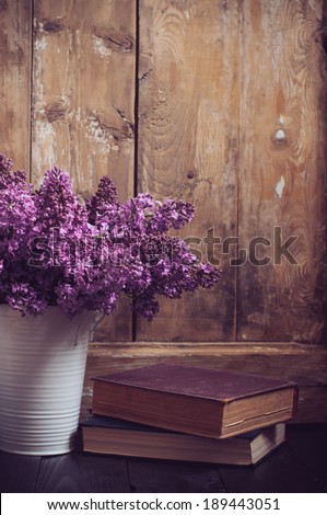 Bouquet of lilac flowers in a pot and old books on a background of vintage wooden board, home decor in a rustic style