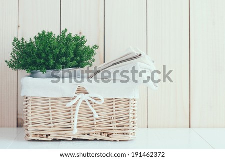 Home decor: vintage wicker basket, house plant and a stack of linen napkins on a wooden board  background, cozy composition retro style, soft pastel colors.