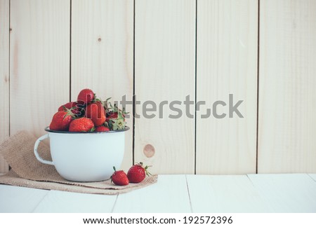 Fresh ripe red strawberries in white enamel mug and rough cloth on wooden background, natural rustic food