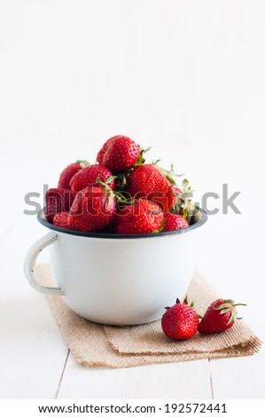 Fresh ripe red strawberries in white enamel mug and rough cloth on a table, natural food background