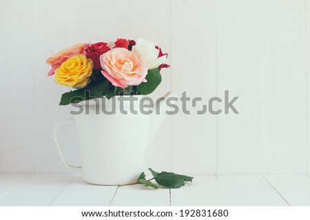 Bouquet of fresh flowers, colorful roses in white enamel coffee pot, home decor in country style, painted white background